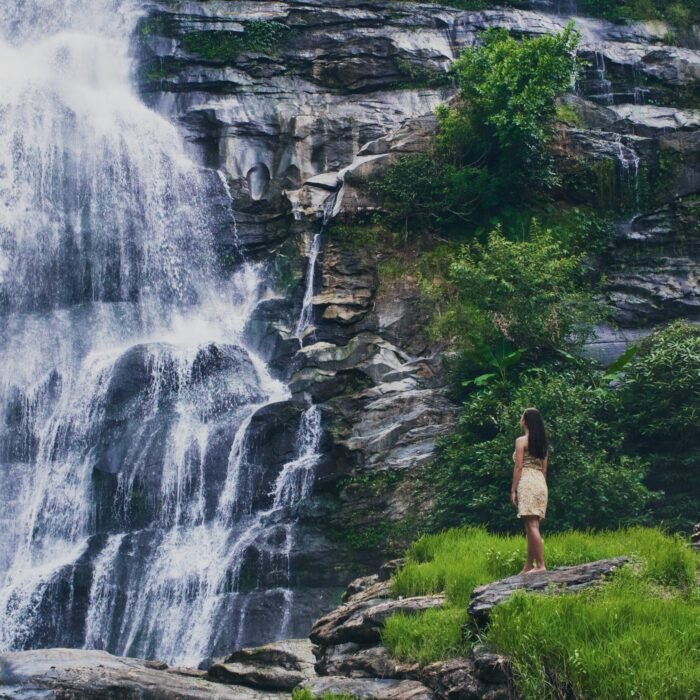 Fascinating low angle shot of a female admiring the waterfall in Doi Inthanon park in Thailand